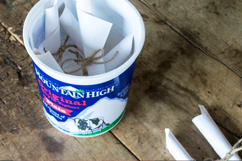A Mountain High Yoghurt pot that has been cleaned out and now has bundles of paper wrapped up in twine inside and beside it for the bucket list craft.