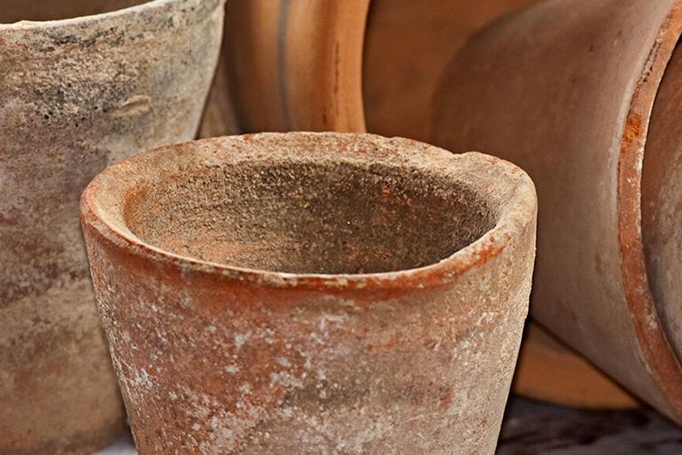 A small pot made of ceramic standing upright, behind it are several other ceramic pots in various positions, one standing, others tipped over.